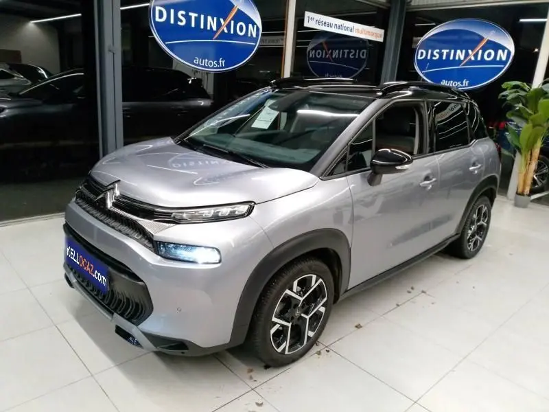Vue 3/4 avant d'un Citroën C3 Aircross gris 2022 avec toit noir et jantes alliage distinctives en intérieur showroom.