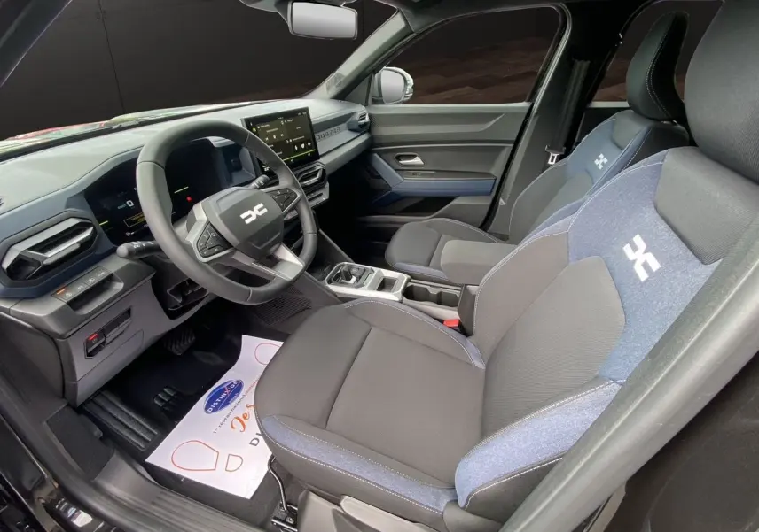 Intérieur avant droit du Dacia Duster hybride 2025, sièges tissu noir et bleu avec logo distinctif sur appuie-tête.