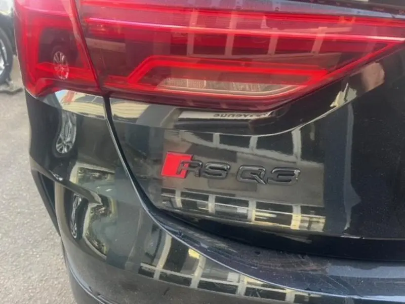 Gros plan sur le feu arrière gauche et le logo RS Q3 rouge et noir du coffre d'une Audi RS Q3 Sportback noir Mythic.