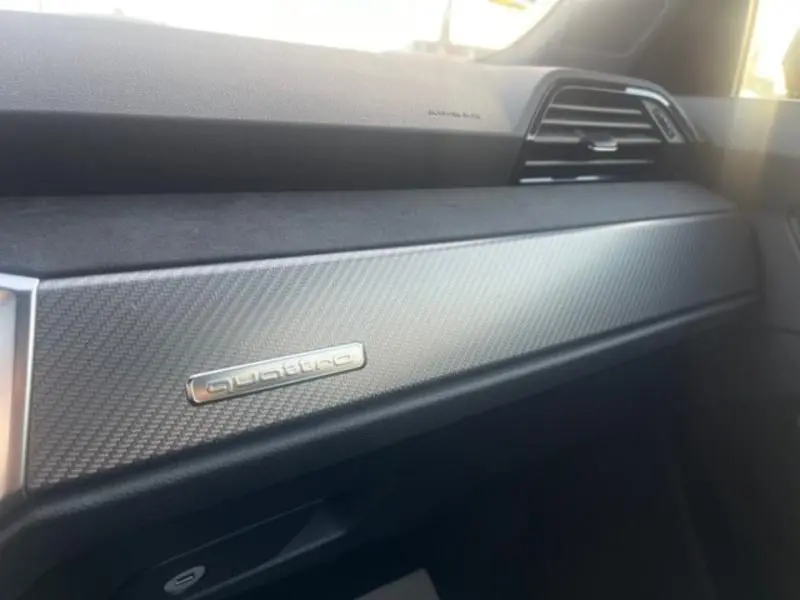 Détail intérieur côté passager avec insert carbone et logo quattro sur le tableau de bord d'Audi RS Q3 Sportback noir Mythic.