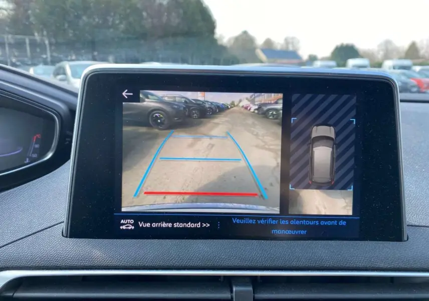 Écran de la Peugeot 3008 blanc montrant l'aide au stationnement arrière avec caméra et guidage graphique bleu et rouge.