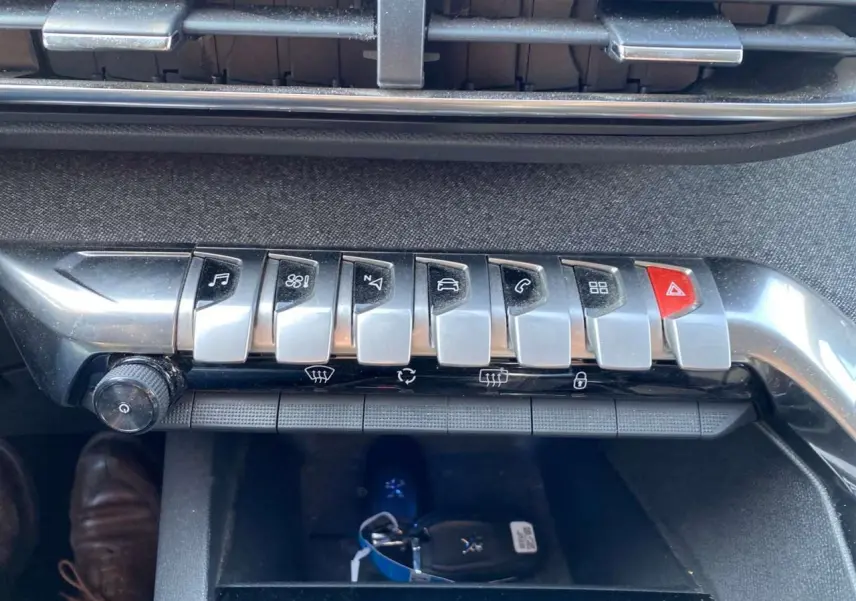 Gros plan sur la rangée de boutons chromés de la console centrale du Peugeot 3008 blanc, avec la clé posée dessous.