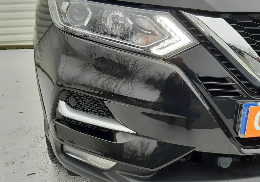 Gros plan sur l'avant droit noir d'un Nissan Qashqai 2020, mettant en valeur le phare LED allumé et la calandre chromée.