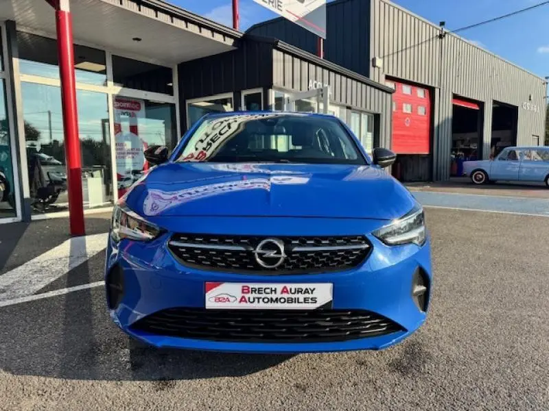 Vue frontale d'une Opel Corsa 1.2 Turbo 100ch Elegance en bleu voltaïque métallisé garée devant un garage.