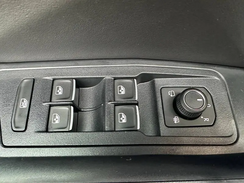 Gros plan sur les commandes de lève-vitres et réglage des rétroviseurs côté gauche du Volkswagen T-Roc gris 2025.
