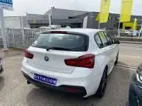 BMW Série 1 114d M Sport blanche vue de 3/4 arrière droit, avec feux arrière LED et double sortie d'échappement.