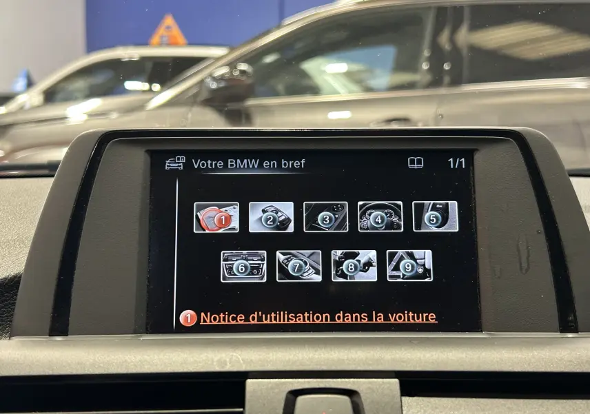 Écran central de la BMW Série 1 gris 2014 affichant le menu d'aide avec plusieurs icônes, vue intérieure frontale.