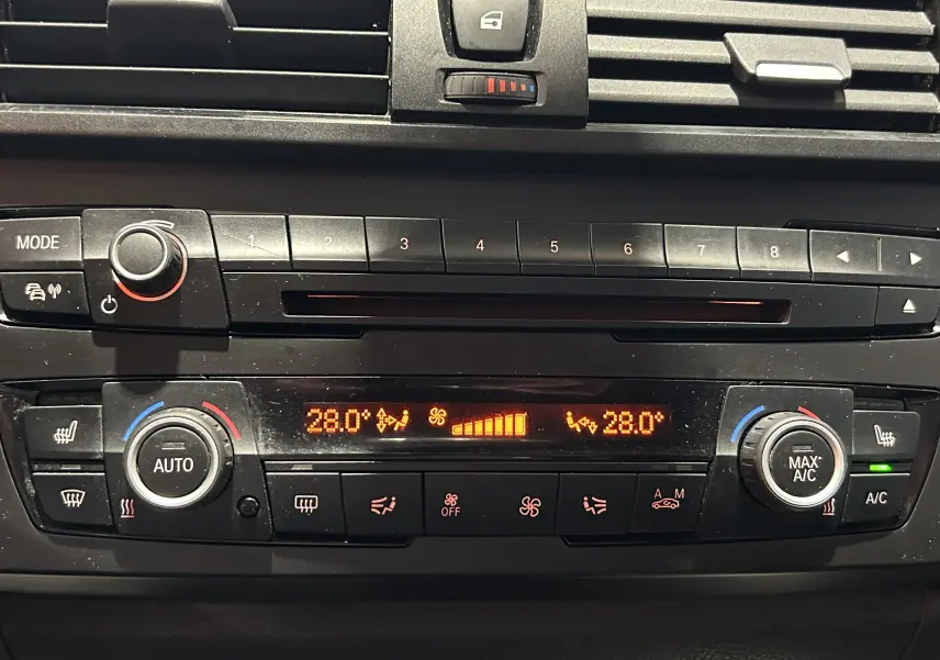 Tableau de bord de BMW Série 1 gris 2014, vue rapprochée sur la console de climatisation digitale affichant 28°C.