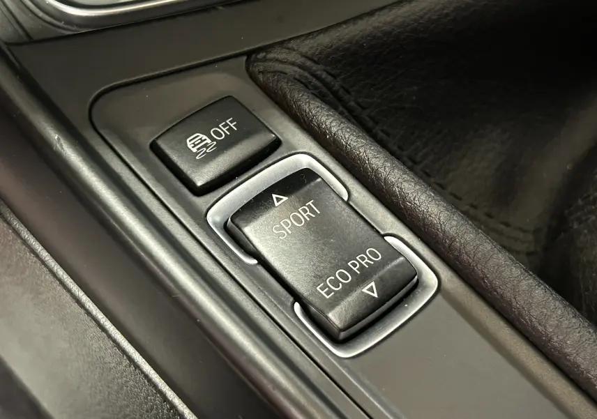 Gros plan sur les boutons de mode de conduite Sport et Eco Pro dans la console centrale d'une BMW Série 1 gris diesel.