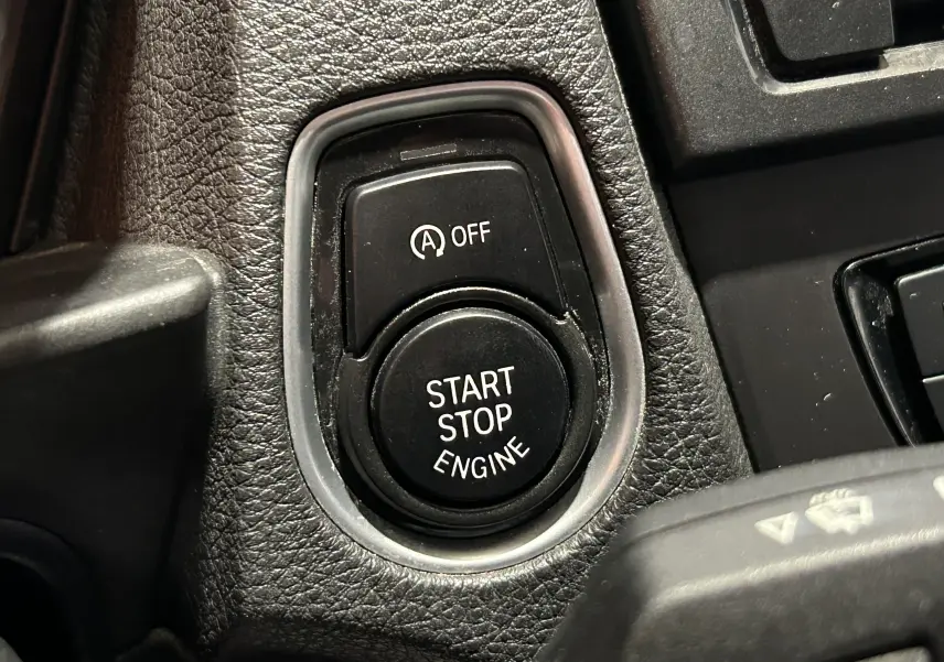 Gros plan sur le bouton Start Stop Engine et la commande d'arrêt automatique sur le tableau de bord noir d'une BMW Série 1 gris diesel.