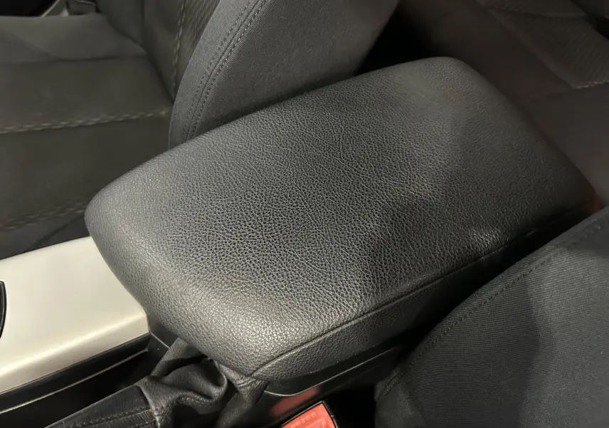 Gros plan sur l'accoudoir central en cuir noir et siège tissu côté conducteur d'une BMW Série 1 gris diesel 2014.