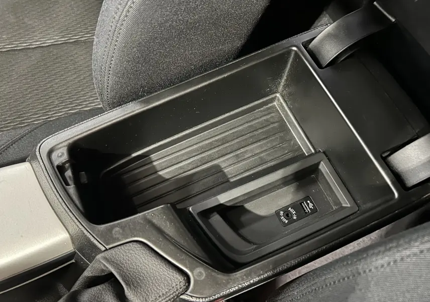 Gros plan sur la console centrale noire de la BMW Série 1 gris, montrant les ports USB et AUX entre les sièges avant.
