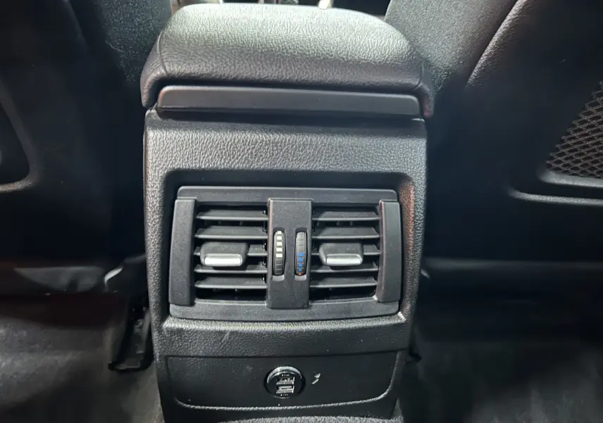 Gros plan sur la console arrière noire avec bouches d'aération et ports USB de la BMW Série 1 gris 2014.