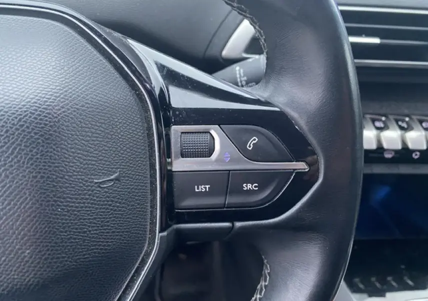 Gros plan sur les commandes au volant noir du Peugeot 3008 blanc, version Allure 2017, avec tableau de bord en arrière-plan.