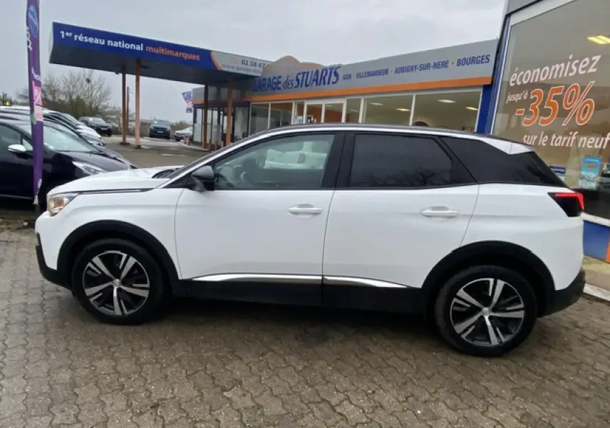 Profil côté gauche du Peugeot 3008 blanc avec toit noir et jantes alliage 18 pouces, stationné devant un garage.