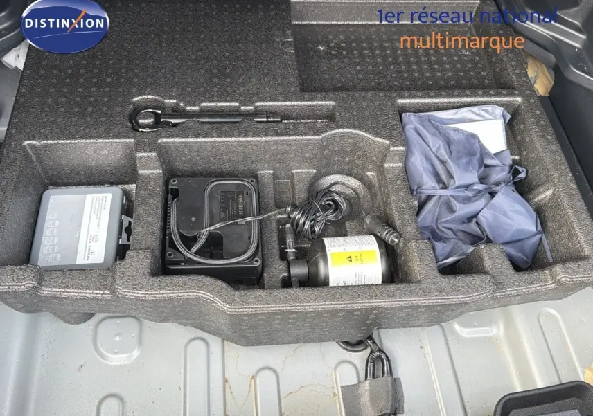 Compartiment de rangement sous le coffre de la Toyota Yaris Cross gris minéral, montrant outils et kit de réparation pneus.