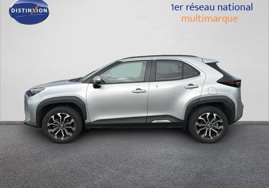 Profil côté gauche de la Toyota Yaris Cross gris minéral avec jantes bi-ton et protections noires sur les passages de roue.