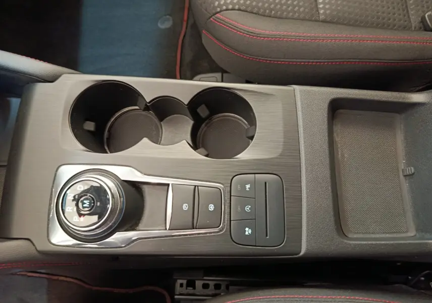 Vue plongeante sur la console centrale noire du Ford Kuga 2024 avec molette de boîte auto et surpiqûres rouges sur sièges.
