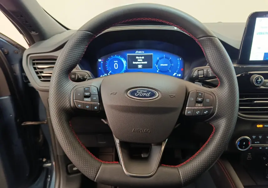 Vue rapprochée du volant en cuir noir avec surpiqûres rouges du Ford Kuga 2024, tableau de bord digital bleu en arrière-plan.