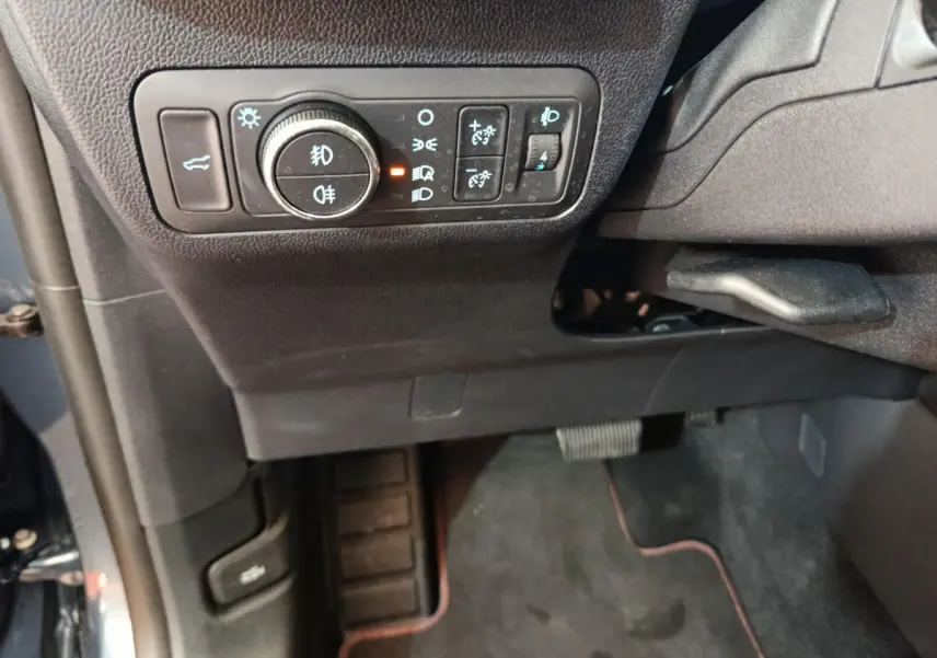 Vue intérieure côté gauche du tableau de bord du Ford Kuga bleu, avec commandes d'éclairage et pédales visibles.