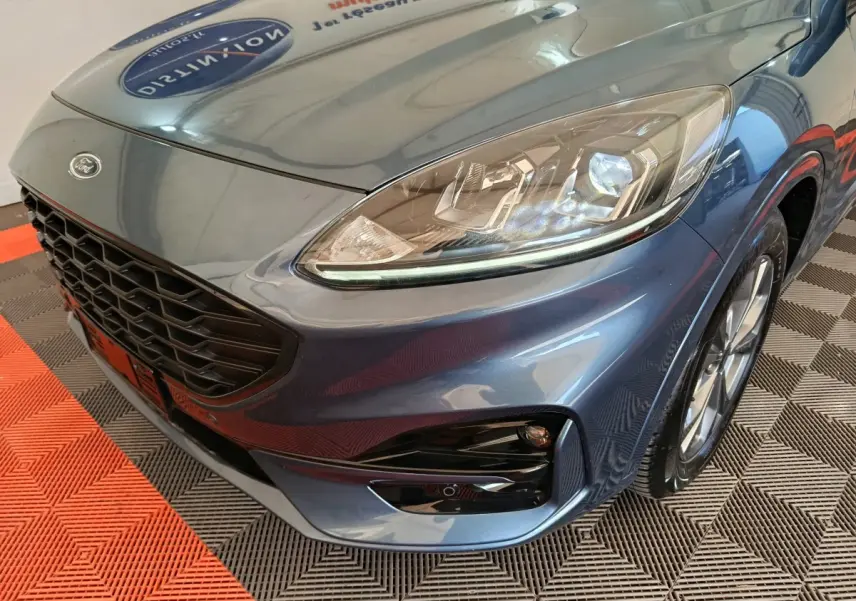 Vue 3/4 avant droit du Ford Kuga bleu 2024, mettant en valeur le phare LED et la calandre noire sportive.