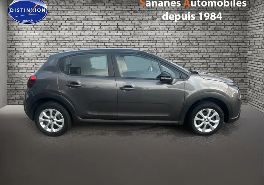 Profil côté droit d'une Citroën C3 gris foncé 2023, avec jantes alliage et rétroviseurs noirs, sur fond brique.