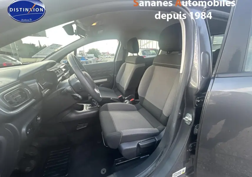 Vue intérieure côté conducteur d'une Citroën C3 gris foncé 2023, mettant en valeur les sièges tissu Mica Grey et la boîte manuelle.