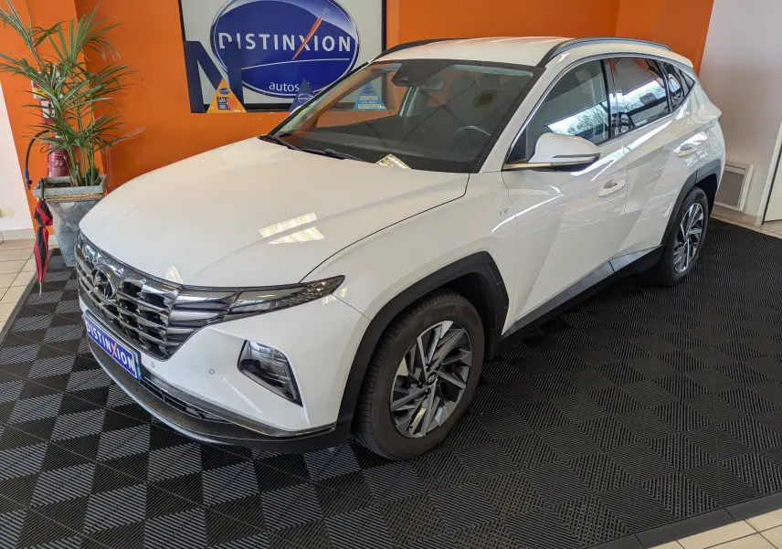 Hyundai Tucson blanc en 3/4 avant droit, avec jantes alliage et calandre chromée dans un showroom.
