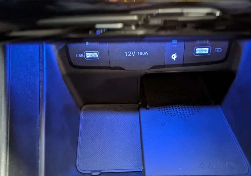 Gros plan sur la console centrale du Hyundai Tucson blanc, montrant les ports USB, prise 12V et chargeur sans fil.