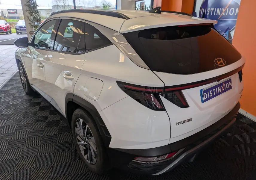 Vue 3/4 arrière droite d'un Hyundai Tucson blanc avec vitres teintées et jantes alliage, en intérieur showroom.