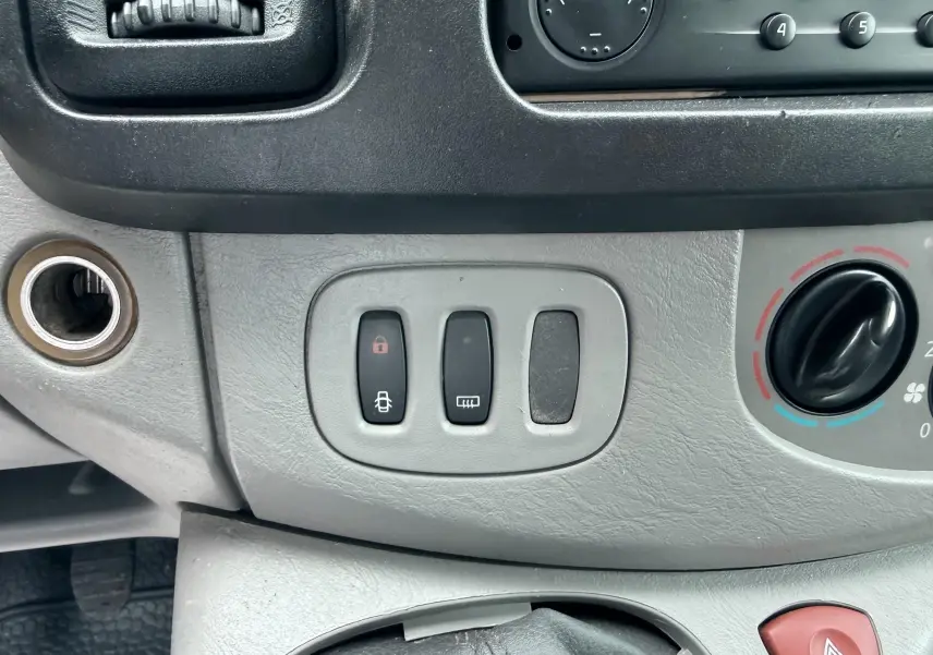 Détail du tableau de bord gris avec commandes de verrouillage et dégivrage sur Nissan Primastar blanc de 2005.