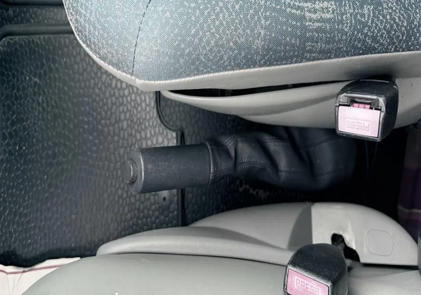Détail intérieur montrant les ceintures de sécurité et frein à main entre les sièges tissu gris-bleu du Nissan Primastar.