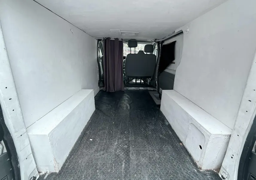 Vue intérieure arrière du Nissan Primastar blanc de 2005, montrant l’espace de chargement vide avec banquettes latérales blanches.