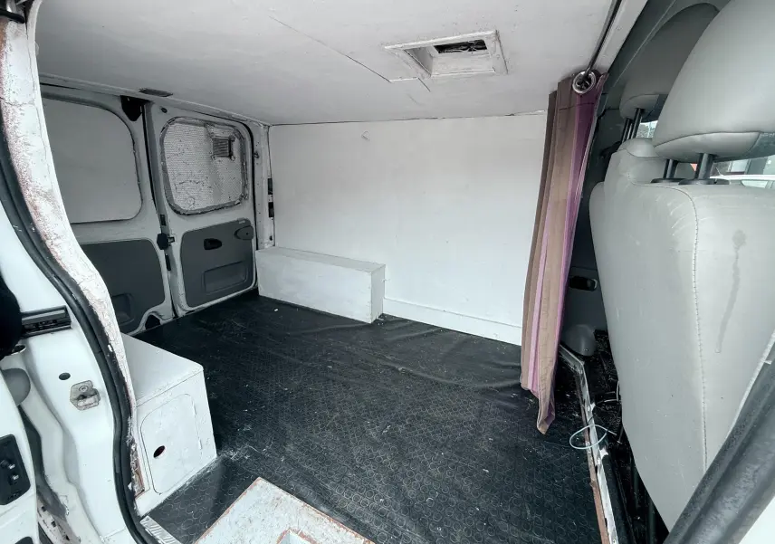 Vue intérieure arrière du fourgon blanc Nissan Primastar 2005 montrant l'espace de chargement vide avec sol noir et sièges gris.