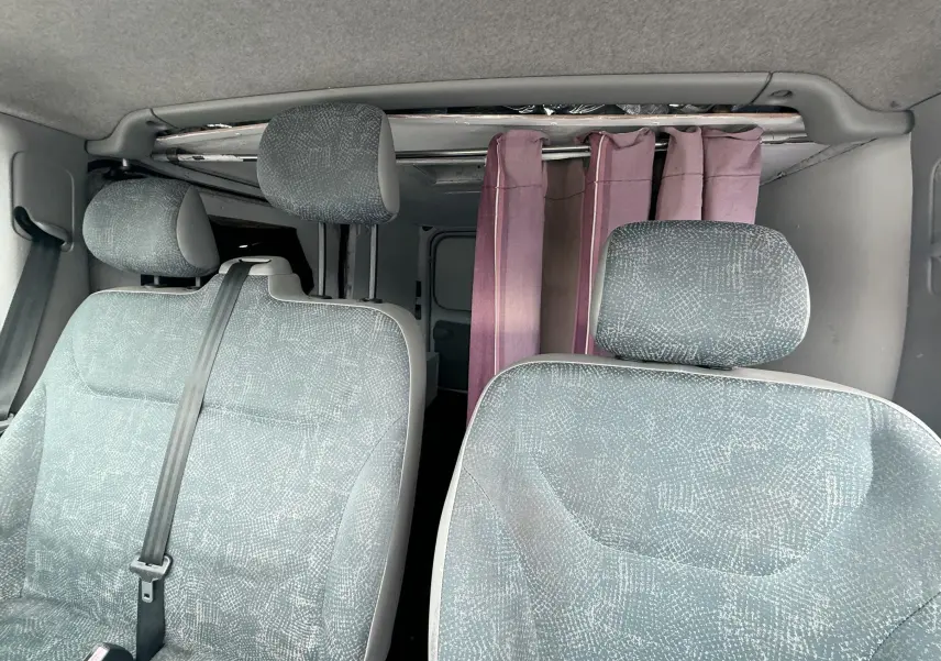 Intérieur du Nissan Primastar 2005, vue avant des sièges gris bleuté avec rideau violet à l'arrière.