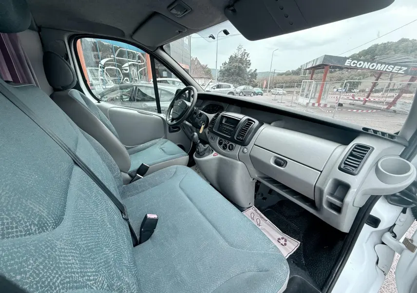 Vue intérieure côté conducteur du Nissan Primastar 1.9 DCI 100 de 2005 avec sièges tissu gris bleu et tableau de bord clair.
