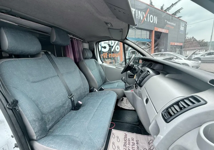 Vue intérieure côté conducteur du Nissan Primastar 1.9 DCI 100 de 2005 avec sièges tissu gris-bleu et tableau de bord gris.