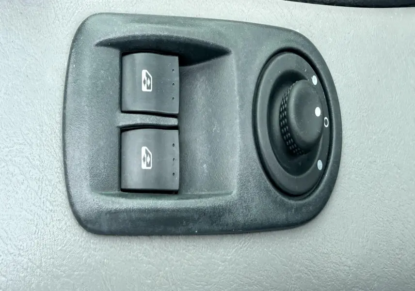 Vue rapprochée des commandes électriques des vitres et du réglage des rétroviseurs sur la portière côté conducteur d’un Nissan Primastar blanc.