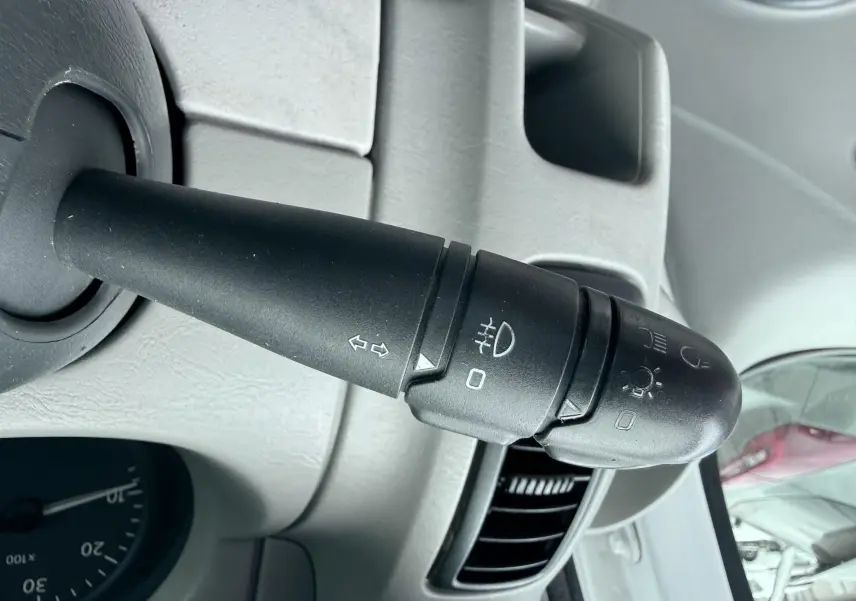 Gros plan sur la manette de clignotants noire à gauche du volant dans l’habitacle gris clair du Nissan Primastar blanc.
