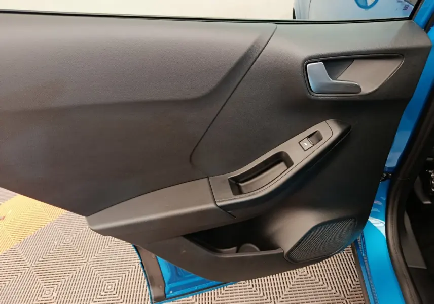 Vue intérieure de la porte avant gauche noire avec poignée et bouton de vitre, cadre bleu visible sur Ford Puma 2025.