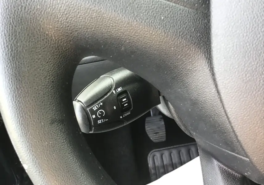 Gros plan sur la commande de régulateur de vitesse derrière le volant noir d'une Peugeot 208 essence 2018.