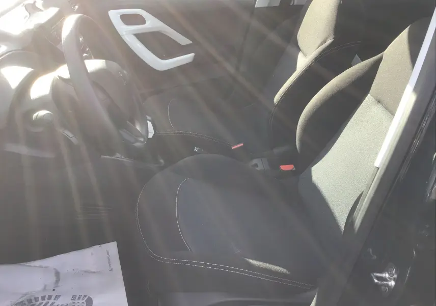 Intérieur de la Peugeot 208 essence 2018, vue côté conducteur, sièges noirs avec surpiqûres blanches, volant visible.