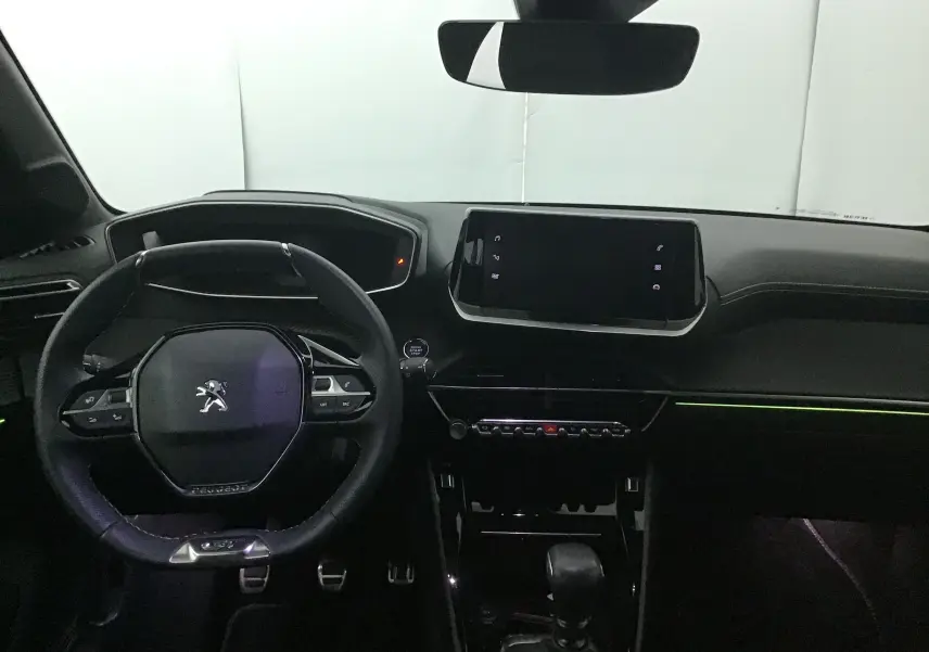 Intérieur Peugeot 208 2023 vue du poste de conduite, volant compact et écran tactile central, ambiance sombre avec éclairage d’ambiance.