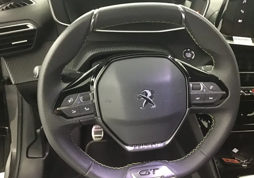 Volant cuir noir avec surpiqûres vertes du Peugeot 208 GT 2023, vue rapprochée du poste de conduite intérieur.