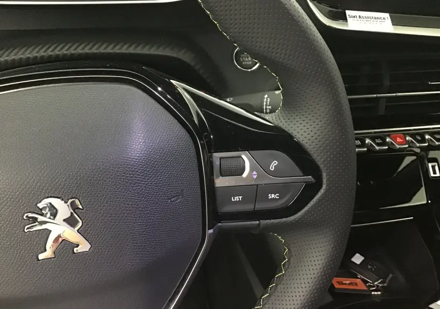 Gros plan sur le volant cuir perforé côté droit du Peugeot 208 gris platinium/noir avec commandes audio intégrées.