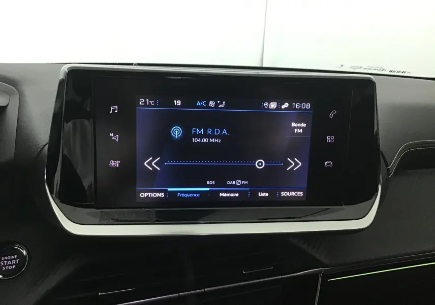 Écran tactile central allumé dans l'habitacle noir du Peugeot 208 GT 1.2 PureTech 2023, affichant une radio FM.