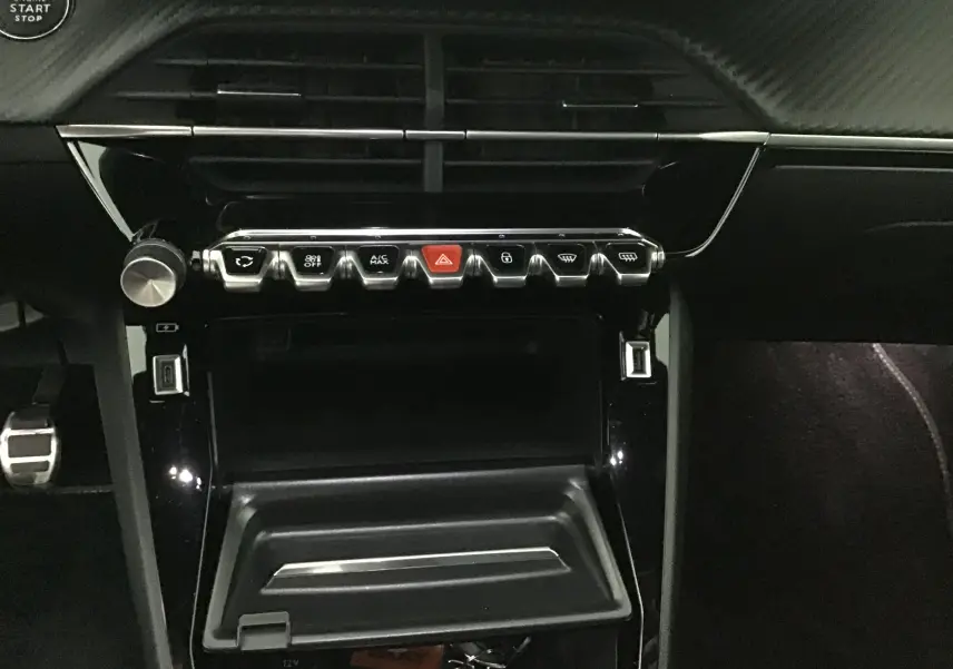 Vue rapprochée de la console centrale noire de la Peugeot 208 1.2 PureTech 100 GT avec boutons chromés et finition carbone.