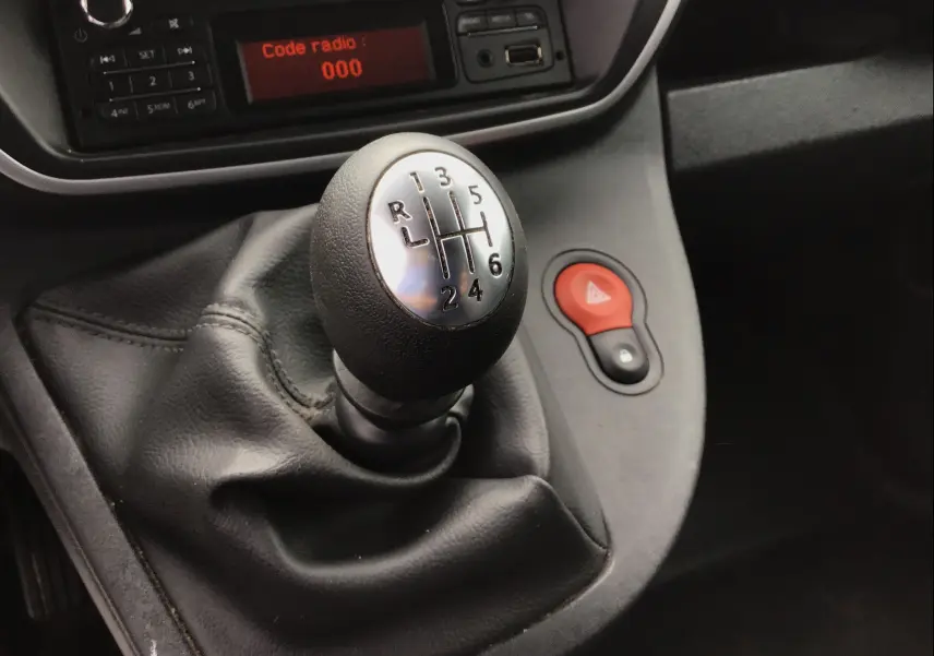 Gros plan sur le levier de vitesses manuel noir du Renault Kangoo blanc 2019, avec tableau de bord et bouton de warning rouge visible.