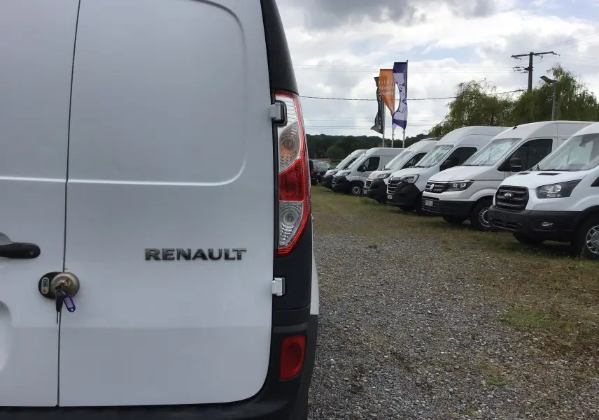 Vue arrière gauche d'un Renault Kangoo blanc 2019 avec serrure et clé visibles, stationné parmi d'autres utilitaires blancs.