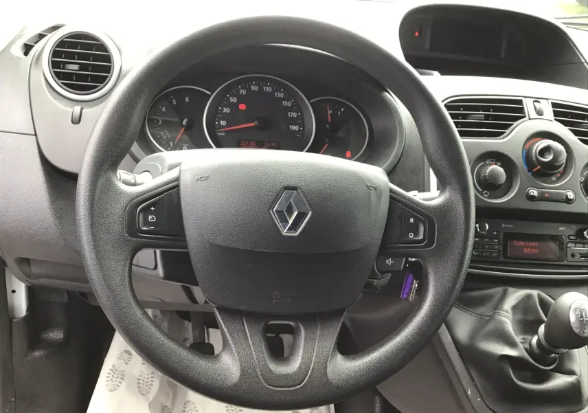 Vue intérieure centrée sur le volant noir Renault avec tableau de bord et console centrale d'un Kangoo blanc 2019.